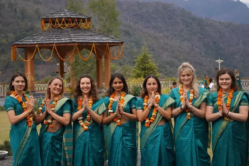 Graduates in green saris with marigold garlands, hands in prayer, at the ashram gazebo