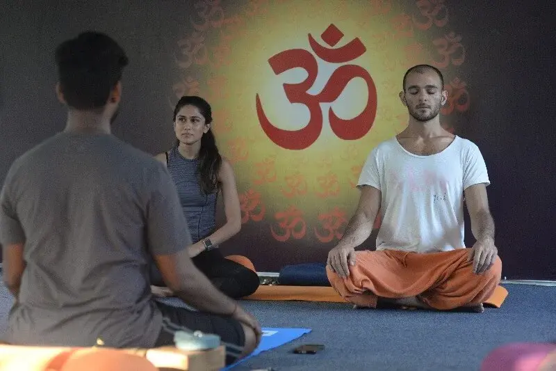 Students meditating in front of an Om backdrop during a guided session