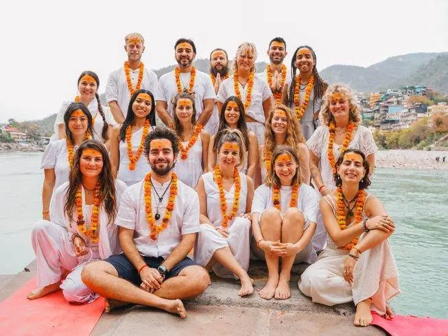 500 hour yoga teacher training graduates with marigold garlands beside the Ganga in Rishikesh