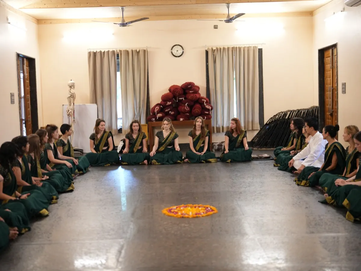 Graduates in green saris sit in a circle around a marigold rangoli at their closing ceremony