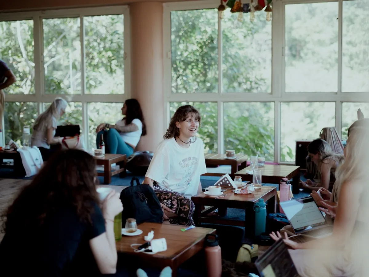 Students talk and study over tea and laptops in the ashram cafe, with forest outside the windows