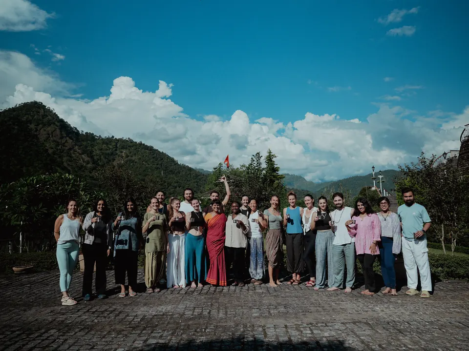 A teacher training batch celebrates together on the ashram terrace beneath the mountains