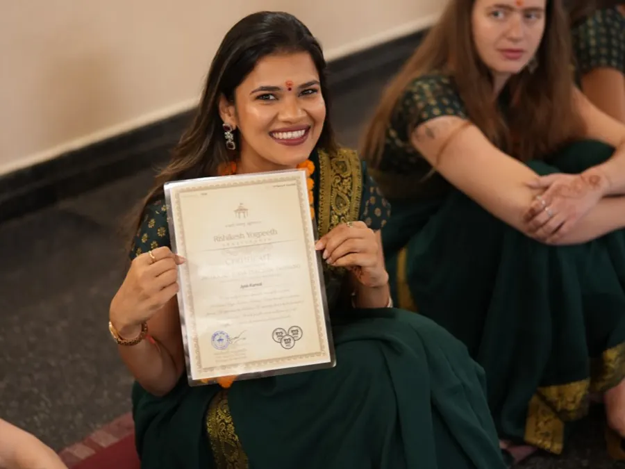 A smiling graduate holds up her teacher training certificate