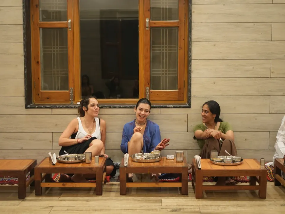 Three students laugh together over dinner at the low tables of the ashram dining hall