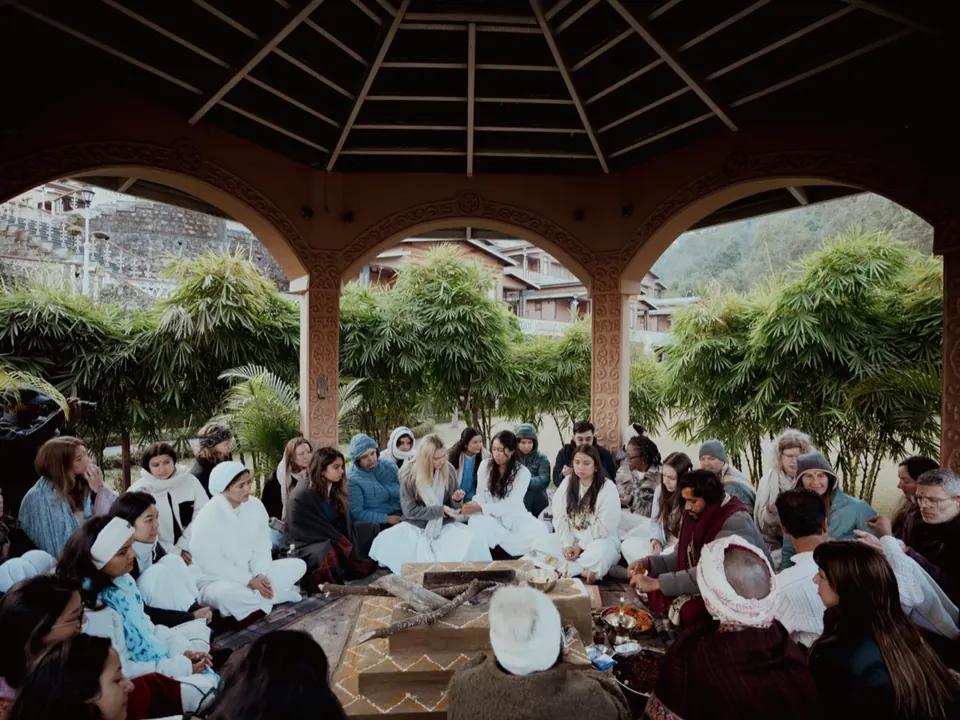 Students sit together around the havan fire in the garden pavilion