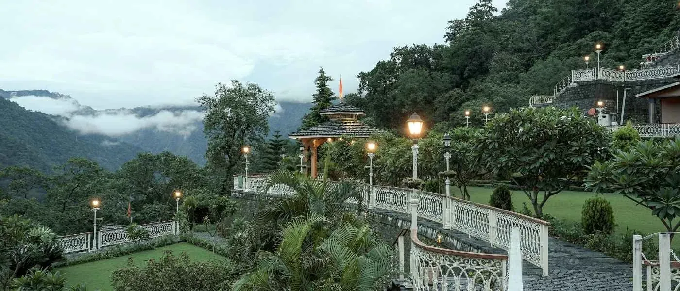 Ashram garden and walkways at dusk with the Himalayan foothills behind