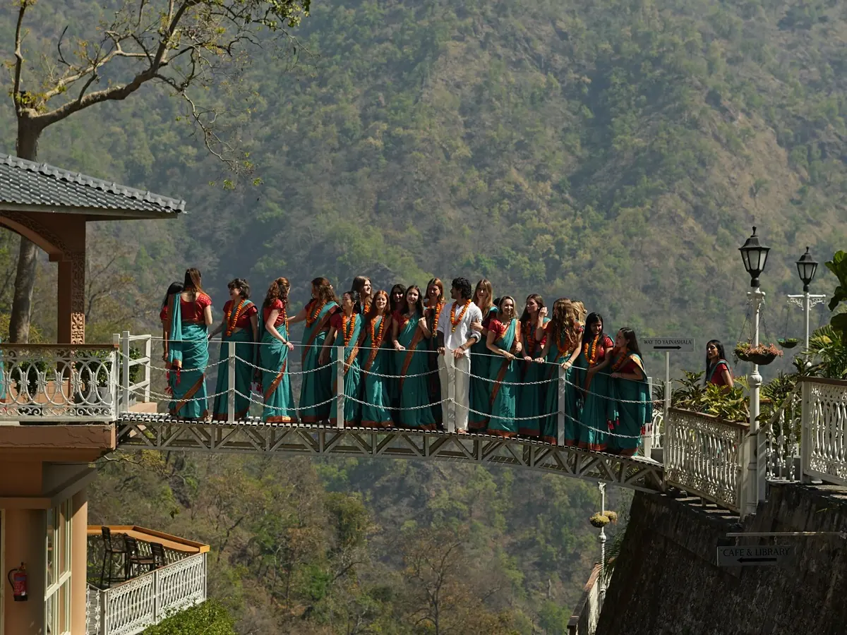 A graduating class in saris stands together on the ashram bridge above the forested valley