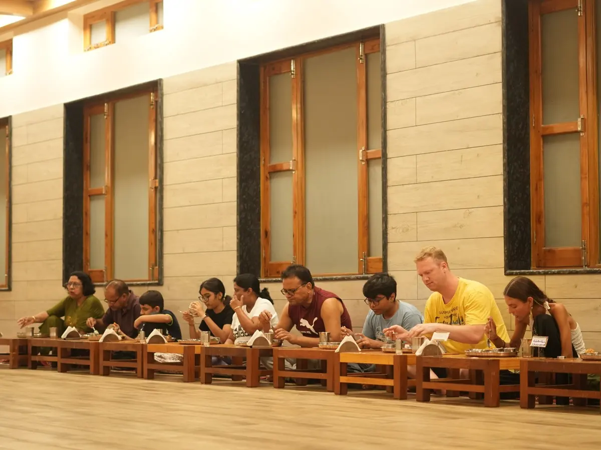 Guests of different ages share a vegetarian meal at the low tables of the dining hall