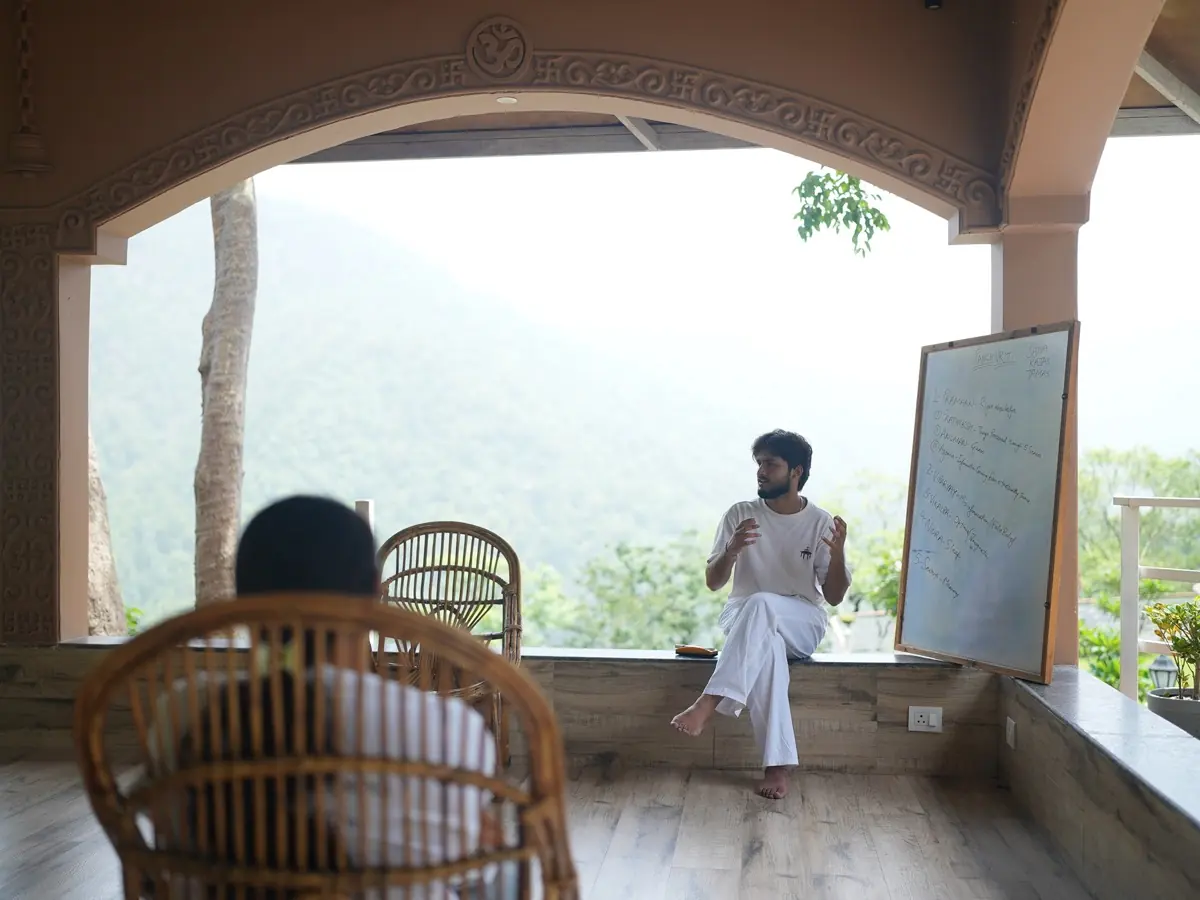 A teacher talks with students in the open stone pavilion, with a whiteboard and forested hills behind