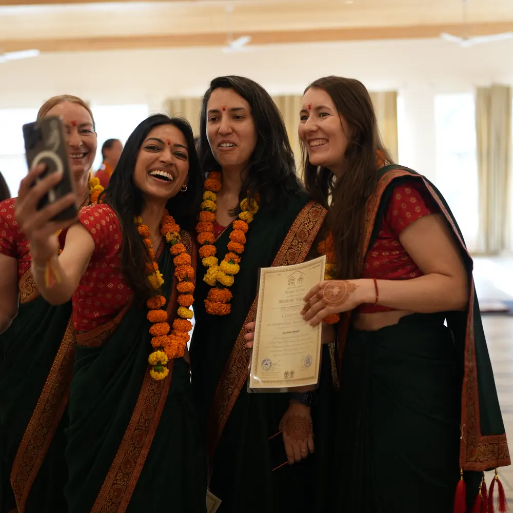 Four graduates in saris and marigold garlands take a selfie together, one holding her teacher training certificate