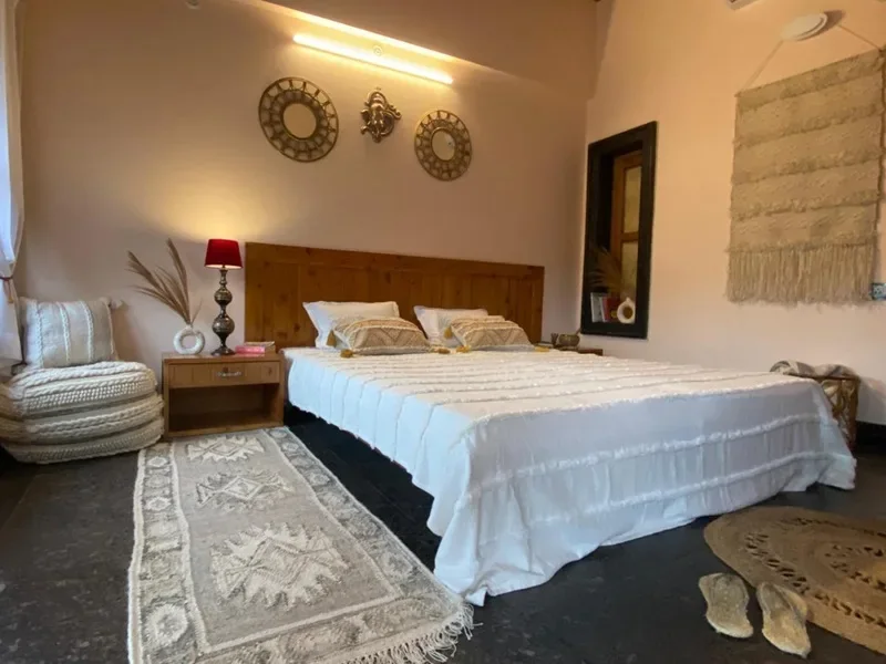 Bright ashram bedroom with a double bed, woven rugs and handcrafted wall decor