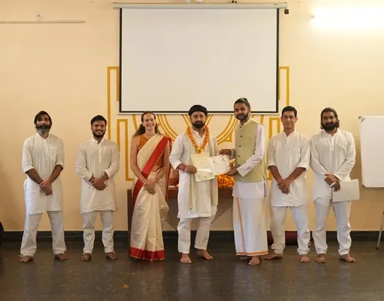 A graduate receiving a course certificate from the faculty at Rishikesh Yogpeeth