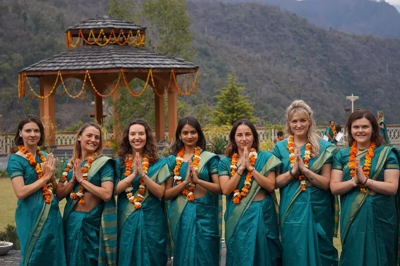 Yoga teacher training students in teal saris and marigold garlands with hands in prayer at Abhayaranya Yoga Ashram