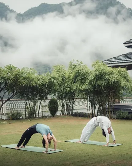 Two students in wheel pose on the lawn with misty mountains behind