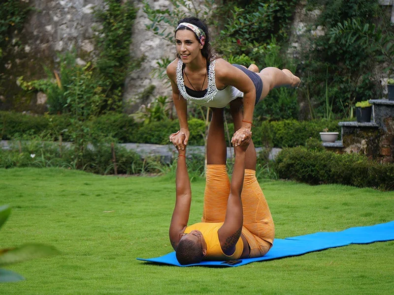 Two students practising partner acro yoga on the ashram lawn